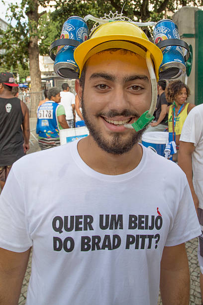 Street Carnival in Rio Rio de Janeiro, Brazil - March 1, 2014: Young man wears a helmet with two beer cans connected with a tube to your mouth,  His teeshirt says, in portuguese: do you want a kiss from Brad Pitt ? nudie suit stock pictures, royalty-free photos & images