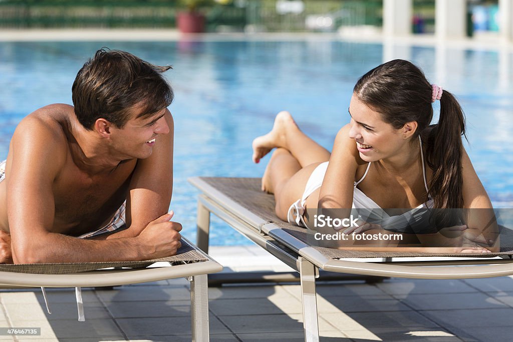 Young couple talking by the swimming pool Young man and woman lying down on deck chairs by the swimming pool, talking. Relaxation Stock Photo