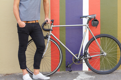 Cropped shot of a stylishly dressed young man standing next to a bicycle against a colourful background