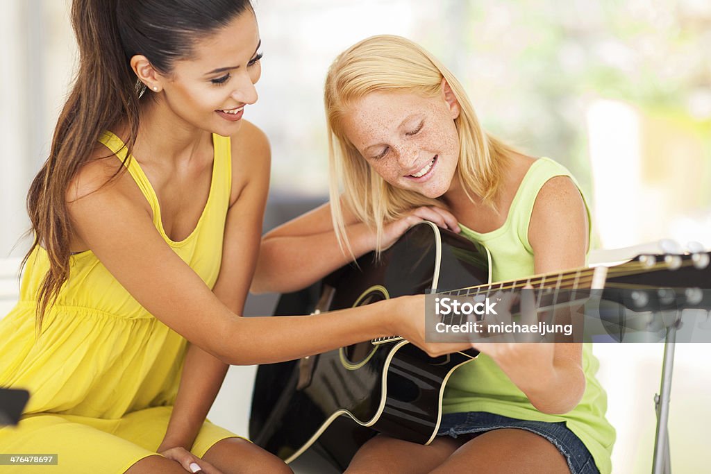 beautiful music teacher tutoring young girl to play guitar smiling beautiful music teacher tutoring young girl to play guitar Assistance Stock Photo