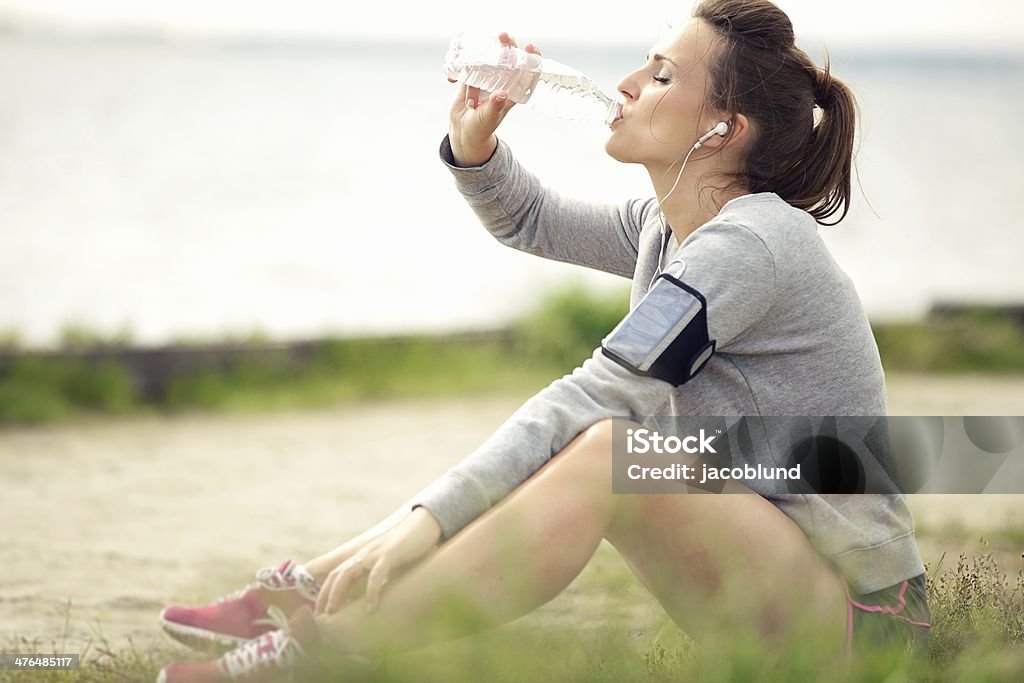 Femmina Jogger di riposo e bere acqua in bottiglia - Foto stock royalty-free di Ambientazione esterna