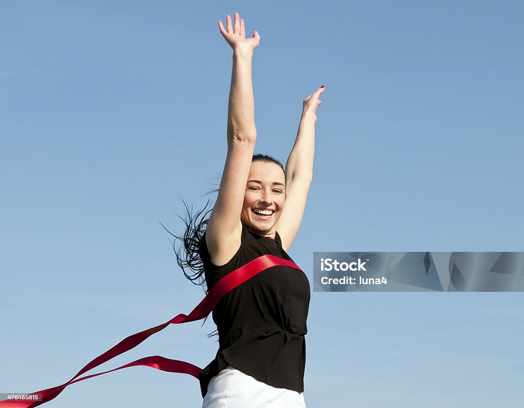 businesswoman crossing the finish line happy smiling young business woman crossing  red finish line ribbon, against blue sky Finish Line Stock Photo