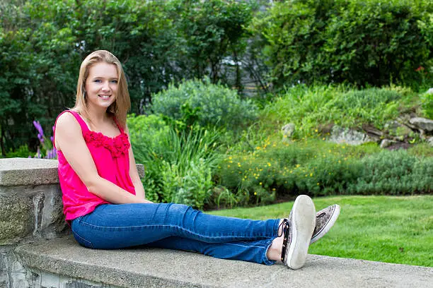 Teenage Girl sitting on block wall with flower garden in background