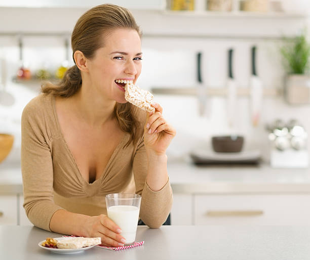 istock Young woman eating snacks in modern kitchen 476495397