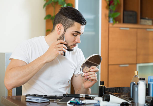 istock guy looking at mirror and shaving beard with trimmer 476495520
