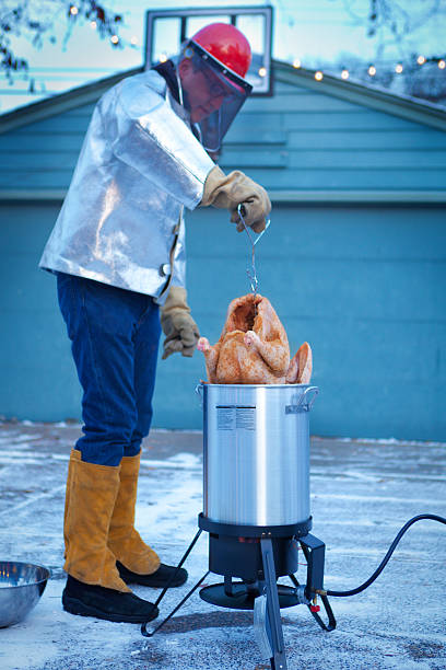 Deep Frying Turkey in Hot Oil for Christmas and Thanksgiving The process of deep frying a turkey in boiling hot oil. A golden brown turkey lifted by the lifting hook from the hot oil. A popular preparation method for turkey dinner for the holiday season of Christmas and Thanksgiving in United States. Photographed in vertical format. deep fried photos stock pictures, royalty-free photos & images