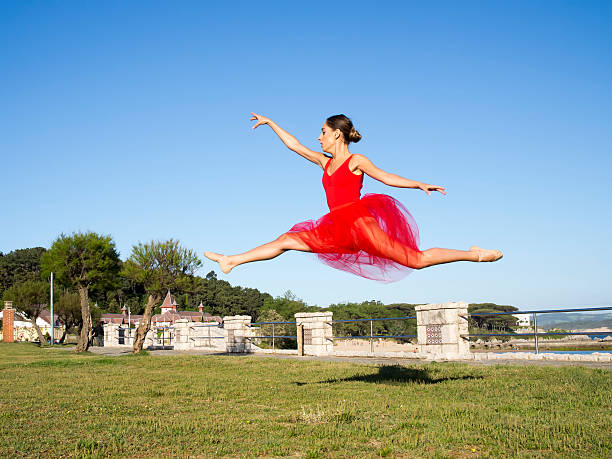 large jump of beautiful ballet dancer in urban park at summer wearing red