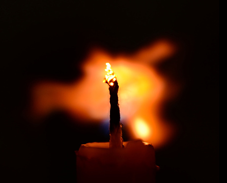 A macro photo of a red candle with no people and dark background. The orange flame of the candle is being blown off showing clearly the burning wick.