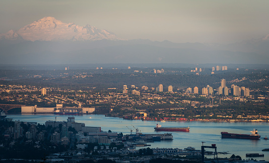 Vancouver, Canada - June 6, 2015: An aerial or elevated perspective view of Vancouver, British Columbia's busy Burrard Inlet. Tanker, bulk and container shipping vessels are active in the foreground, while urban areas of east Vancouver, Burnaby and Surrey are visible in the background. Looming above in the distance is Mount Baker, located in Washington State.