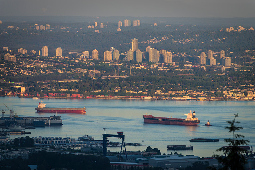 Vancouver, Canada - June 6, 2015: An aerial or elevated perspective view of Vancouver, British Columbia's busy Burrard Inlet. Tanker, bulk and container shipping vessels are active in the foreground, while urban areas of east Vancouver, Burnaby and Surrey are visible in the background.