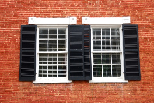 Photograph of a pair of twelve pane windows with black shutters on a red brick house.