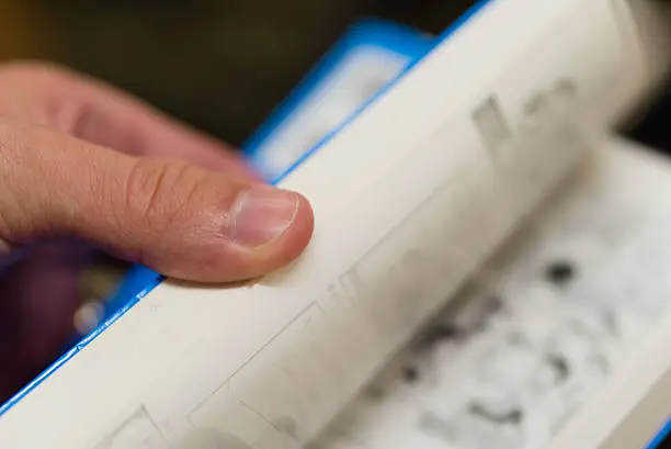 A close up of a hand flipping through the pages of a paperback book.