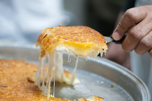 iStockalypse Dubai.  Closeup of a baker’s hand pulling freshly baked Middle Eastern, Palestinian Kunafa pastry made with cow’s milk clarified butter, noodle threads and cheese in a commercial kitchen.  For sale at a bakery in Dubai, UAE, Middle East, GCC.