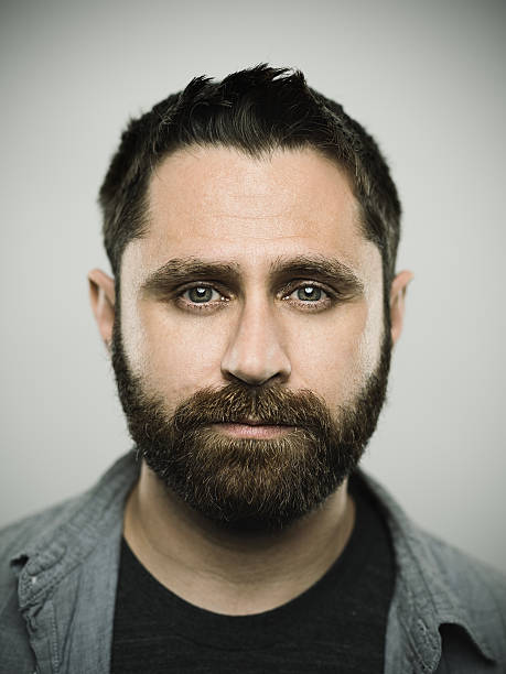 Portrait of a caucasian real young man Portrait of a real caucasian young man with neutral expression. Brown eyes and hair with beard. 35 years old north american. Vertical color image from a dslr camera in studio. blank expression photos stock pictures, royalty-free photos & images