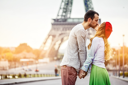 Photo of young loving couple kissing in front of the Eiffel tower in Paris, France.
