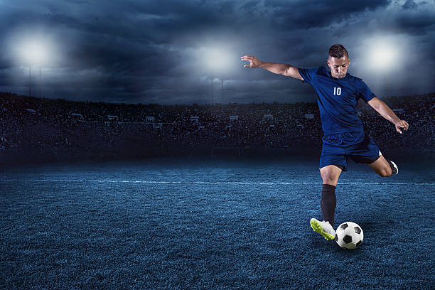 Soccer player kicking ball in a large stadium at night Action photo of professional soccer or football player during game in full floodlit stadium at night offense sporting position photos stock pictures, royalty-free photos & images