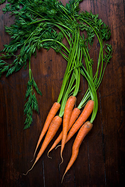 Bunch of fresh carrots with green leaves over wooden background stock photo
