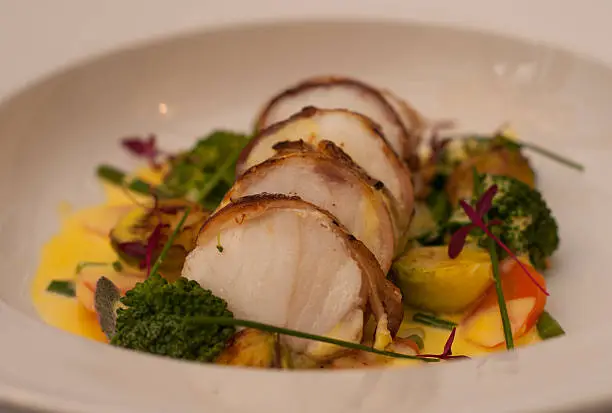 Monkfish, roasted wrapped in pancetta and served in a bowl with seasonal vegetables and a saffron jus.