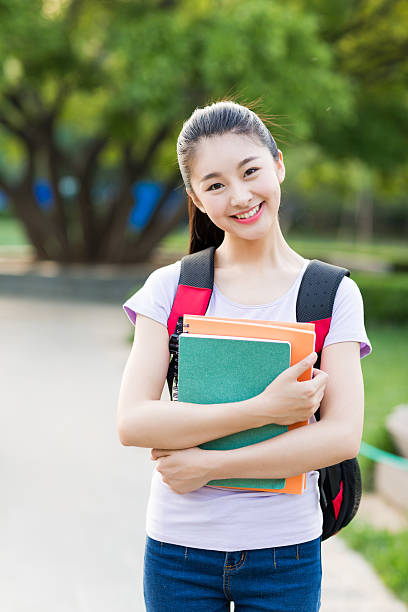 female student outdoors holding a notebook and smiling stock photo
