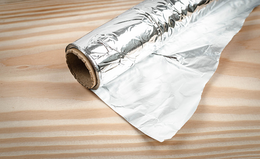 Rolled up aluminum foil on a rustic wooden table. 