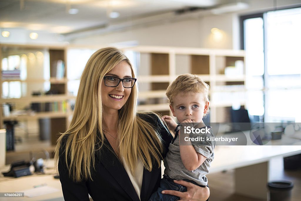 Businesswoman with small child in the office Reconciliation of family and work life: Attractive blond woman in business attire proudly carrying a small boy in her arm in office environment Child Stock Photo
