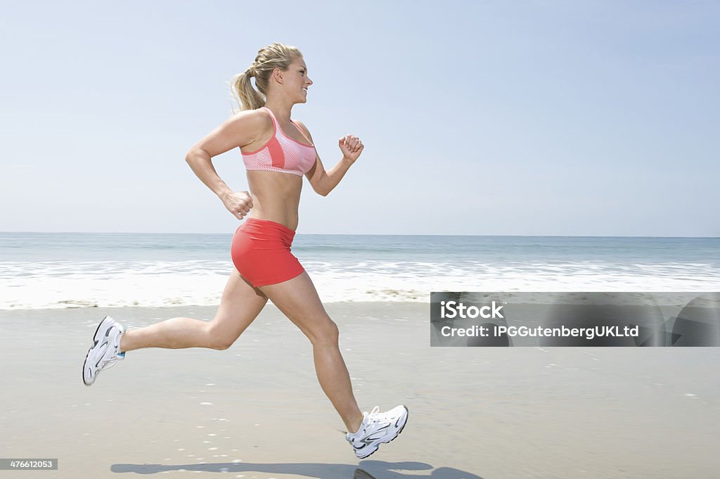 Woman Jogging At Seashore Full length of healthy young woman jogging on seashore Active Lifestyle Stock Photo