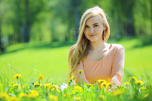 Beautiful young woman laying in spring park with dandelion flowers