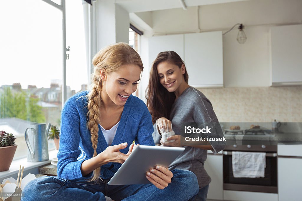 Girl using digital tablet Roommates lifestyle. Blond girl showing something on a digital tablet to her friend. Kitchen Stock Photo