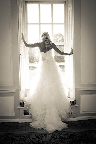 Bride standing looking through a long sash window stock photo