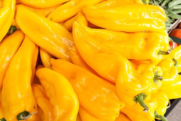 Golden Marconi sweet yellow peppers piled on produce bench at grocery store