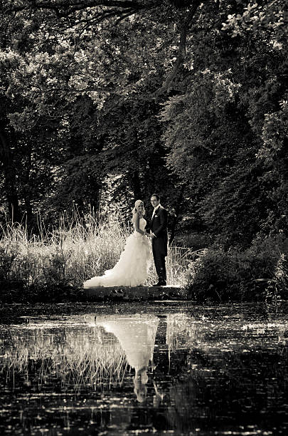 Bride and groom holding hands with reflection during summers day stock photo