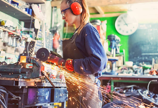 Woman working with an angle grinder Young woman cutting a metal rod with an angle grinder in her workshop. She is wearing protective gloves, goggles and ear muffs. grinding metal power work tool stock pictures, royalty-free photos & images