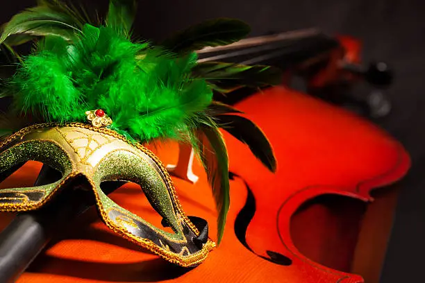 Close-up of Venetian mask with green feathers on violoncello with the black background
