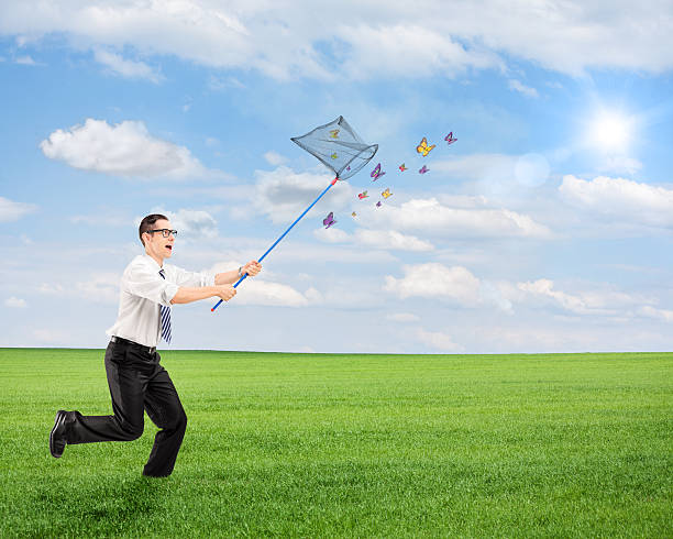 istock Man running and catching butterflies with net on a field 476654073