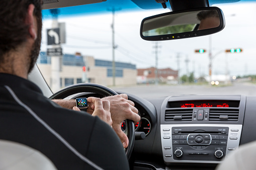Montreal, Сanada - June 7, 2015: Man wearing and using a 42mm 316L Stainless Steel Apple Watch while driving a car. The Apple Watch became available April 24, 2015 and is the latest device produced by Apple.
