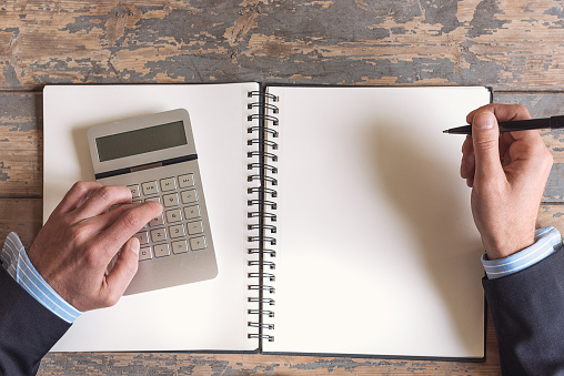 high angle view on business man with calculator and pen on blank office book on rustic old table