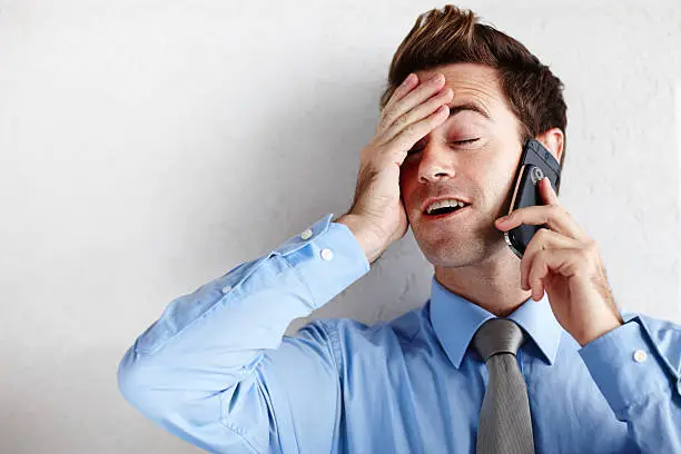 A relieved young businessman rubbing his face while taking a call