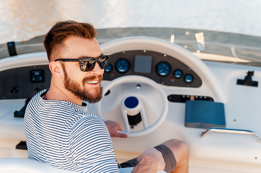 Smiling young man holding hand on steering wheel while driving yacht