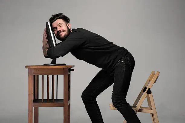 Funny and crazy man using a computer on gray background. human hands hug monitor. Concept of love to computer