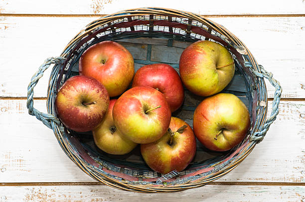Red apples in basket on white wooden background
