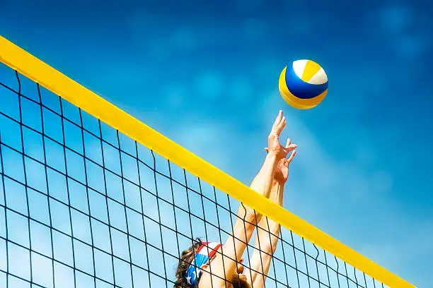 Beachvolley ball player jumps on the net and tries to  blocks the ball