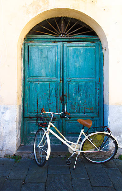 Retro-Style Yellow Bike, Old Tuscan Green Doors, Italy A pale yellow retro-style bike parked near old arched green doors in Lucca, Tuscany, Italy. Some copy space on the black pavement at the bottom of the frame. lucca italy stock pictures, royalty-free photos & images