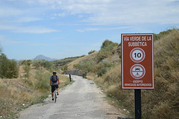 Via Verde in Andalusia, Spain. Photo of a biker on a path moving away from the viewer and sign informing that you are on Green Way (Via Verde). We see only back of the man on bicycle. Landscape of Sierras Subbeticas Natural Park. via verde spain stock pictures, royalty-free photos & images