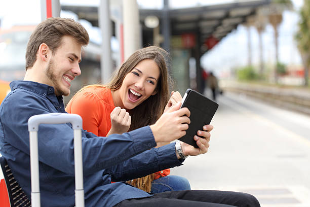 Euphoric couple playing games in a tablet in train station