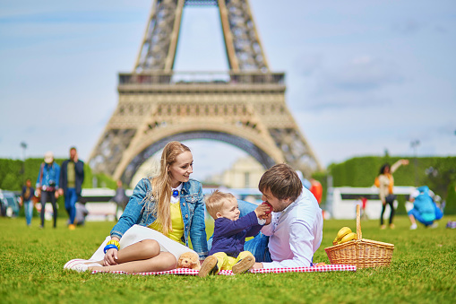 Happy family of three, mother, father and little toddler boy, having picnic in Paris near the Eiffel tower