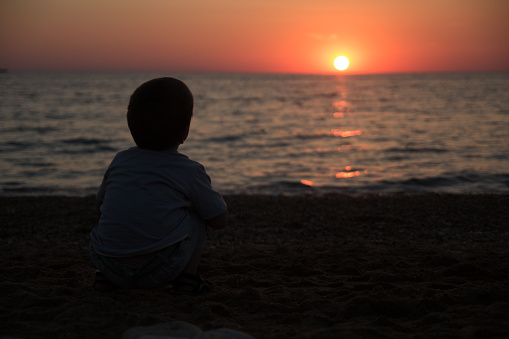 child sitting on his haunches on the beach and enjoy the sunset