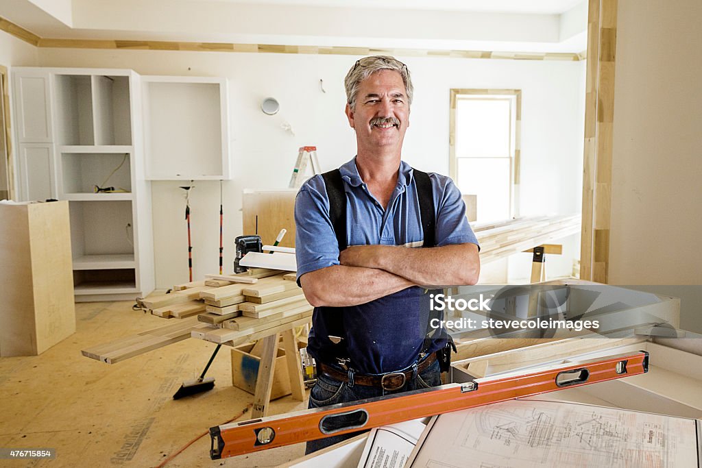 Portrait of Carpenter Portrait of trim carpenter inside home with kitchen cabinets and trim molding in the background. Carpenter age is in his 50s wearing eyeglasses and standing next to blueprints. Building Contractor Stock Photo