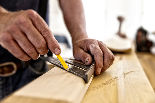 Carpenter using carpenter's square and pencil to mark molding to be cut.