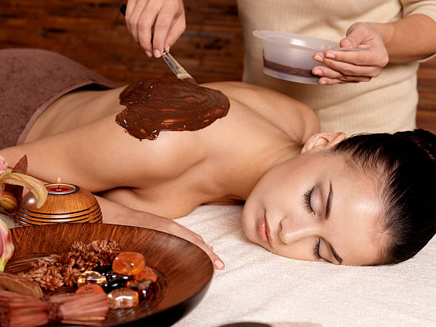 спа терапия для молодых женщин, получающих косметические маски - massaging chocolate spa treatment body стоковые фото и изображения