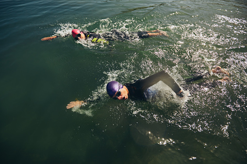 Young Caucasian woman swimming in the sea, while wear swimming goggles, swim cap and swimsuit